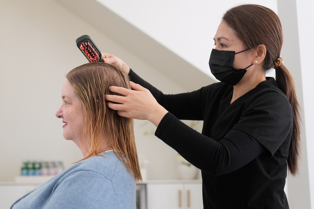Head spa specialist Ha Truong, right, uses a Red and Blue light brush on Liz Evans to help with hair growth and reduce bacteria while massaging the scalp to help the scalp serum absorb during a treatment at Sunday Headspa Thursday, April 16, 2026, in San Francisco. (AP Photo/Jeff Chiu)
