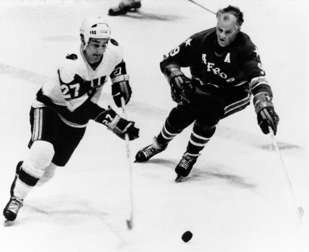 FILE - Gordie Howe, right, of the Houston Aeros, comes in to head Tom Earl of the New England Whalers off from the puck during the first period of the World Hockey Association playoff game in Hartford, Conn., May 11, 1976. (AP Photo/Bob Child, File)