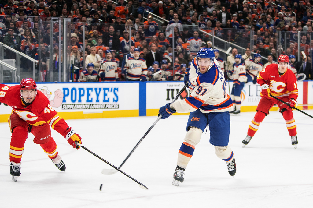 Calgary Flames' Hunter Brzustewicz (48) tries to stop Edmonton Oilers' Connor McDavid (97) from shooting as Flames' Yegor Sharangovich (17) looks on during second period NHL action in Edmonton, Alberta, Tuesday, Dec. 23, 2025. (Amber Bracken/The Canadian Press via AP)