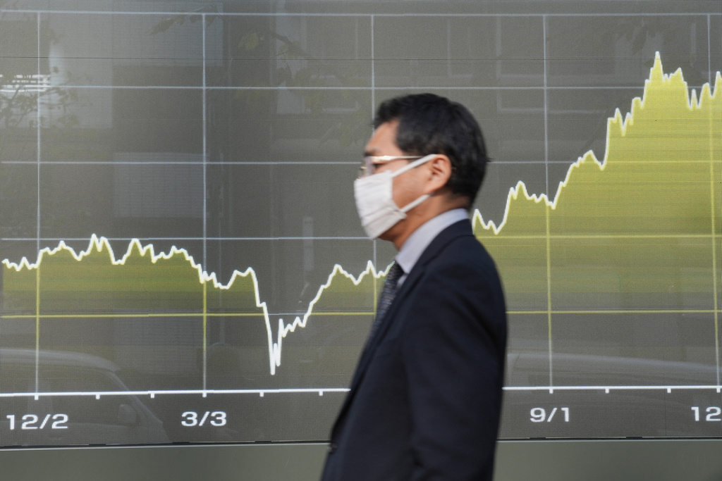 A person walks in front of an electronic stock board at a securities firm Tuesday, Dec. 9, 2025, in Tokyo. (AP Photo/Eugene Hoshiko)