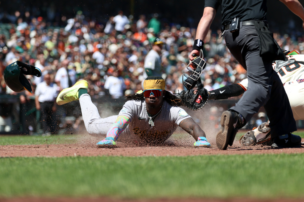 Athletics' Lawrence Butler, center, slides home safe in front of San Francisco Giants catcher Eric Haase (18) on a single hit by Jeff McNeil during the eighth inning of a baseball game in San Francisco, Thursday, June 25, 2026. (AP Photo/Jed Jacobsohn)