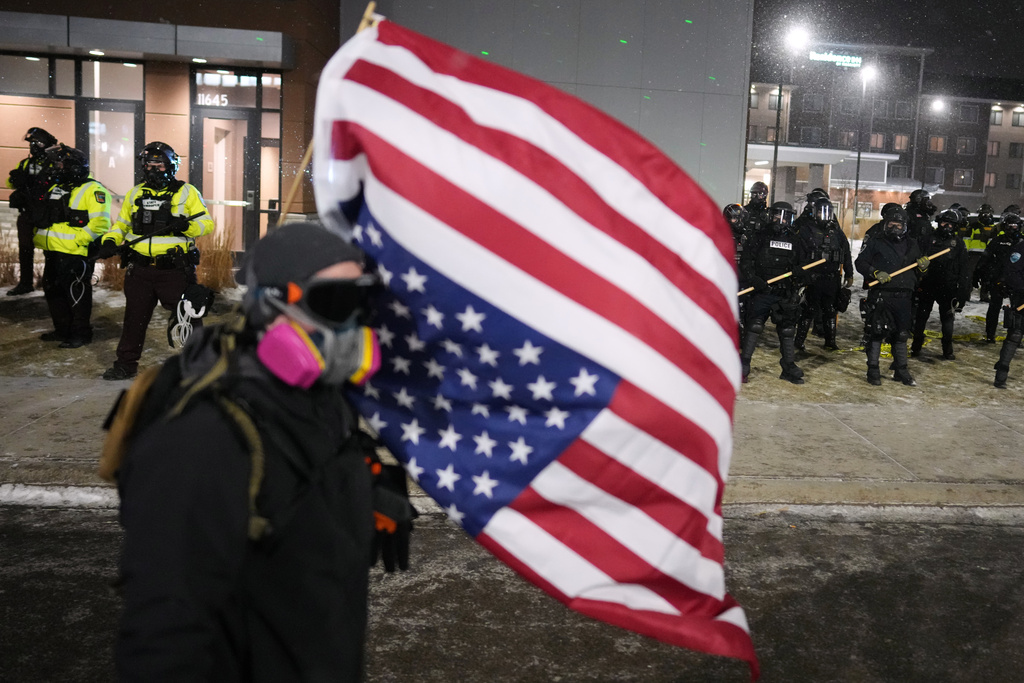 A demonstrator holds an upside-down American flag as law enforcement stand during a protest outside SpringHill Suites and Residence Inn by Marriott hotels on Monday, Jan. 26, 2026, in Maple Grove, Minn. (AP Photo/Adam Gray)