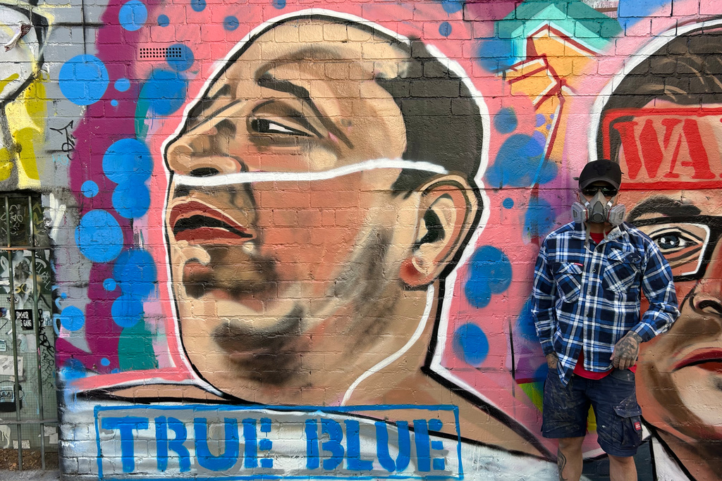 Street artist Jarrod Grech poses for a photo next to his painting of Ahmed al Ahmed, a 43-year-old Syrian-Australian shopkeeper who disarmed one of the attackers of Sydney's Bondi Beach shooting, in Melbourne, Australia, Sunday, Dec. 28, 2025. (Rod McGuirk/AP Photo)