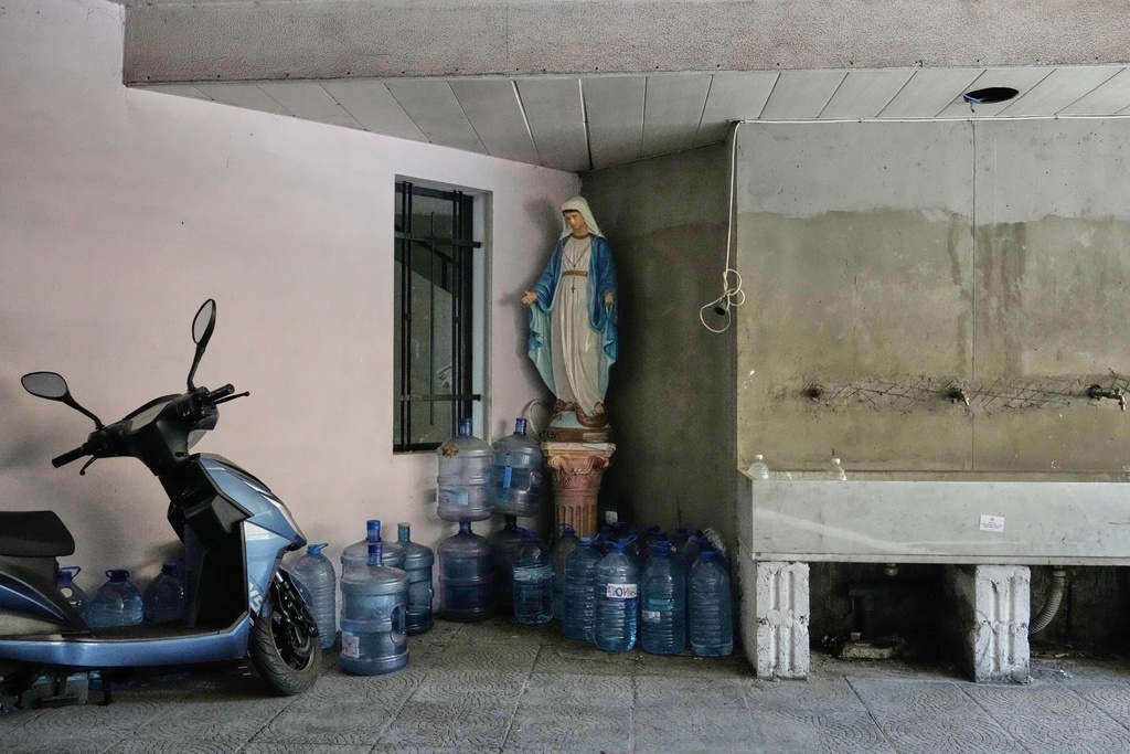 Large water jugs are stacked beside a statue of the Virgin Mary in the corner of a building in Beirut, Lebanon, Monday, Nov. 10, 2025. (AP Photo/Hassan Ammar)