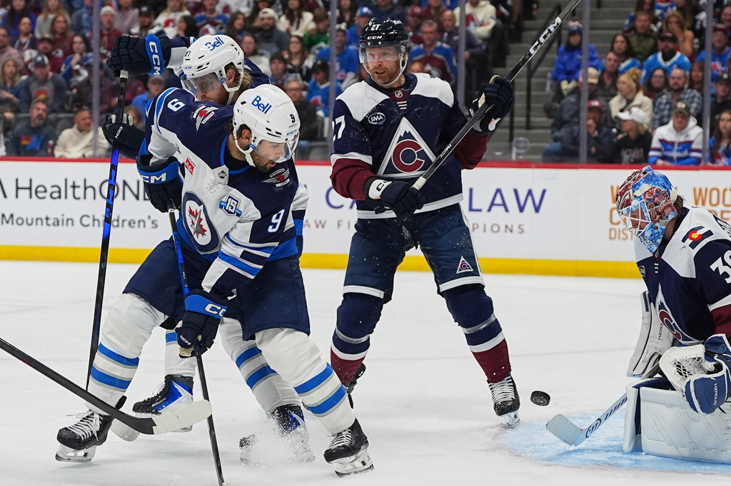 Winnipeg Jets left wing Alex Iafallo (9) shoots the puck past Colorado Avalanche defenseman Brett Kulak (27) as Avalanche goaltender MacKenzie Blackwood, right, makes a stop in the second period of an NHL hockey game Saturday, March 28, 2026, in Denver. (AP Photo/David Zalubowski)