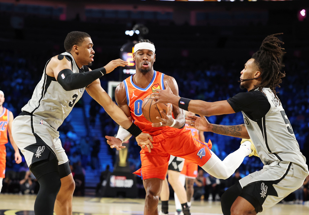 Oklahoma City Thunder guard Shai Gilgeous-Alexander, center, tangles with San Antonio Spurs' Keldon Johnson (3) and Stephon Castle (5) under the net in the first half of an NBA Cup semifinals basketball game, Saturday, Dec. 13, 2025, in Las Vegas. (AP Photo/Ronda Churchill)