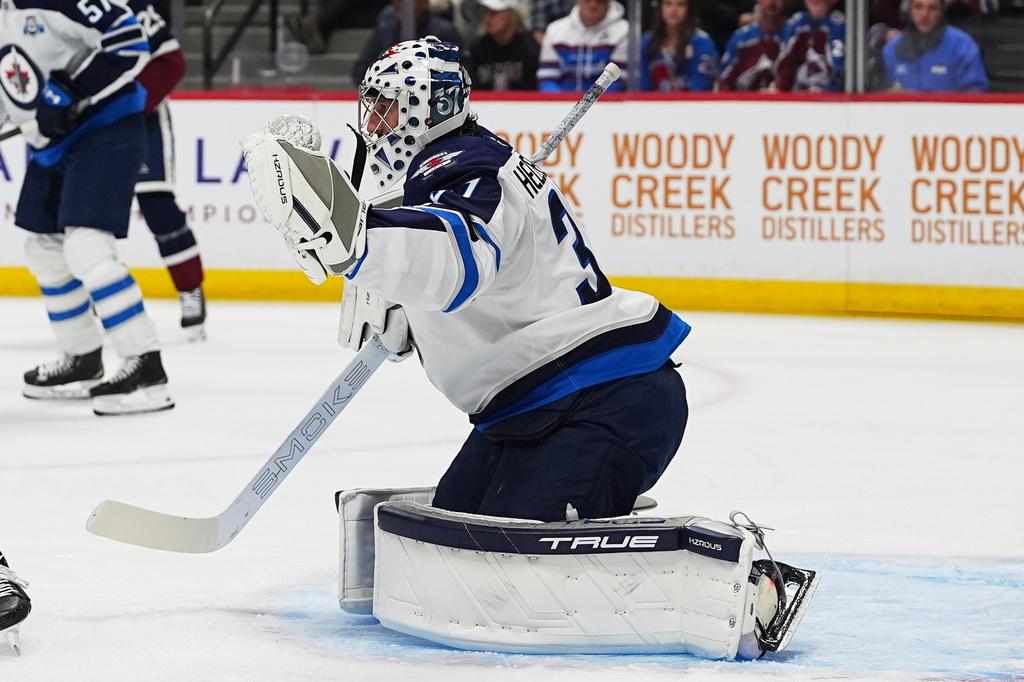 Winnipeg Jets goaltender Connor Hellebuyck makes a glove-save in the first period of an NHL hockey game against the Colorado Avalanche, Saturday, March 28, 2026, in Denver. (AP Photo/David Zalubowski)