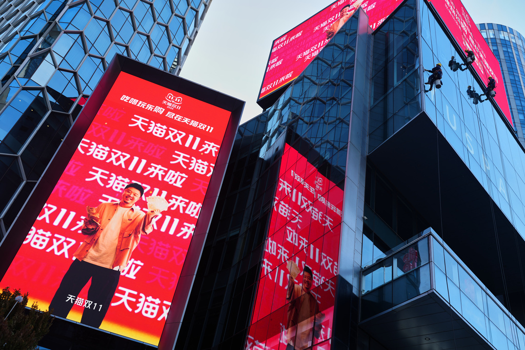 Window cleaners labor an commercial office as an advertisement billboard promoting Tmall's Singles' Day sale at a shopping district in Beijing on Nov. 10, 2025. (AP Photo/Andy Wong)