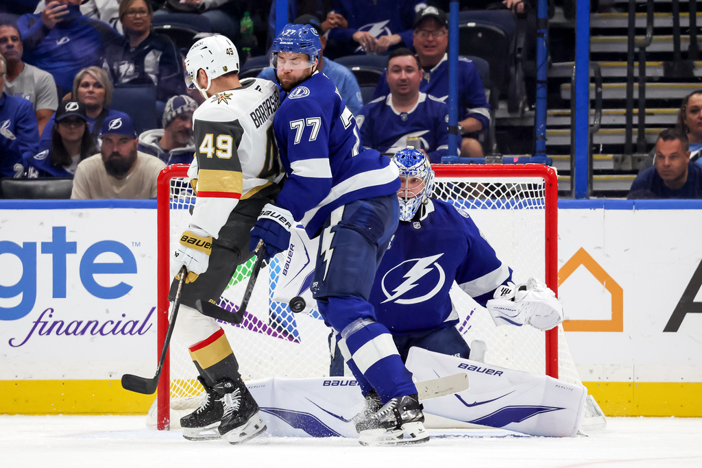 Tampa Bay Lightning goaltender Andrei Vasilevskiy, right, makes a save behind Lightning defenseman Victor Hedman (77) who defends against Vegas Golden Knights' Ivan Barbashev (49) during the second period of an NHL hockey game Sunday, Oct. 26, 2025, in Tampa, Fla. (AP Photo/Mike Carlson)