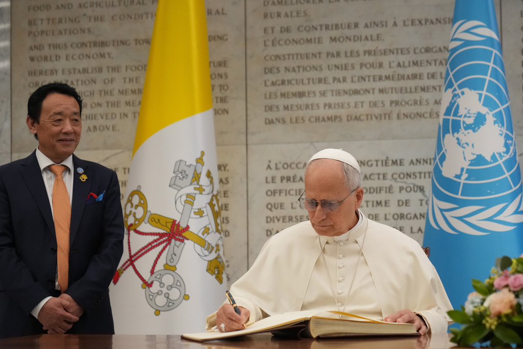 Pope Leo XIV, flanked by FAO Director-General Qu Dongyu, left, signs the FAO Golden Book register of honor as he attends a ceremony marking the 80th anniversary of World Food Day at the FAO headquarters in Rome, Thursday, Oct. 16, 2025. (AP Photo/Alessandra Tarantino)