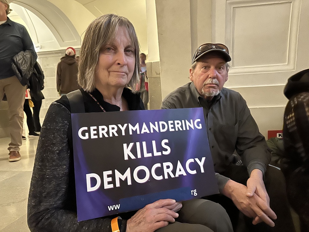 Paula Wood holds a sign protesting Missouri’s congressional redistricting effort while sitting beside her husband, Tim Wood, during a rally on Jan. 21, 2026, at the state Capitol in Jefferson City, Mo. (AP Photo/David A. Lieb)