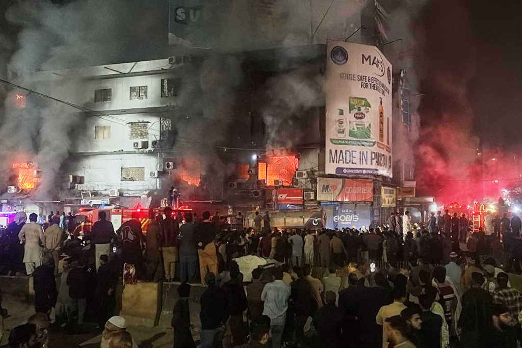 People gather as firefighters try to control a massive fire that broke out in a multi-story shopping mall, in Karachi, Pakistan, Sunday, Jan. 18, 2026. (AP Photo/Mohammad Farooq)