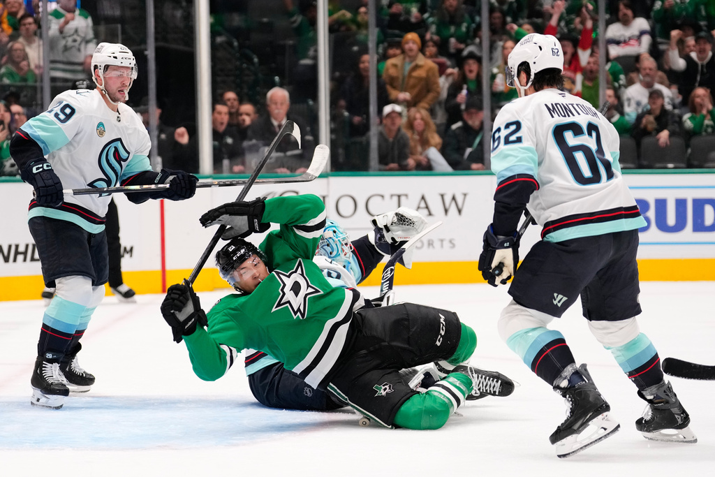 Dallas Stars left wing Jason Robertson falls backwards over Seattle Kraken goaltender Joey Daccord, center rear, as Vince Dunn (29) and Brandon Montour (62) help defend the net in the first period of an NHL hockey game in Dallas, Wednesday, Feb. 25, 2026. (AP Photo/Tony Gutierrez)