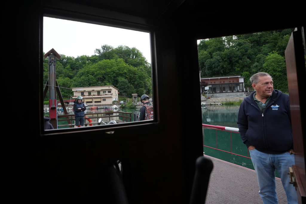 Worker Venanzio Lavelli stands as commuters board the “Da Vinci Ferry,” a hand-operated ferry of a type sketched by Leonardo da Vinci in 1513, on the Adda River between the provinces of Lecco and Bergamo, in Imbersago, Italy, Thursday, June 4, 2026. (AP Photo/Luca Bruno)