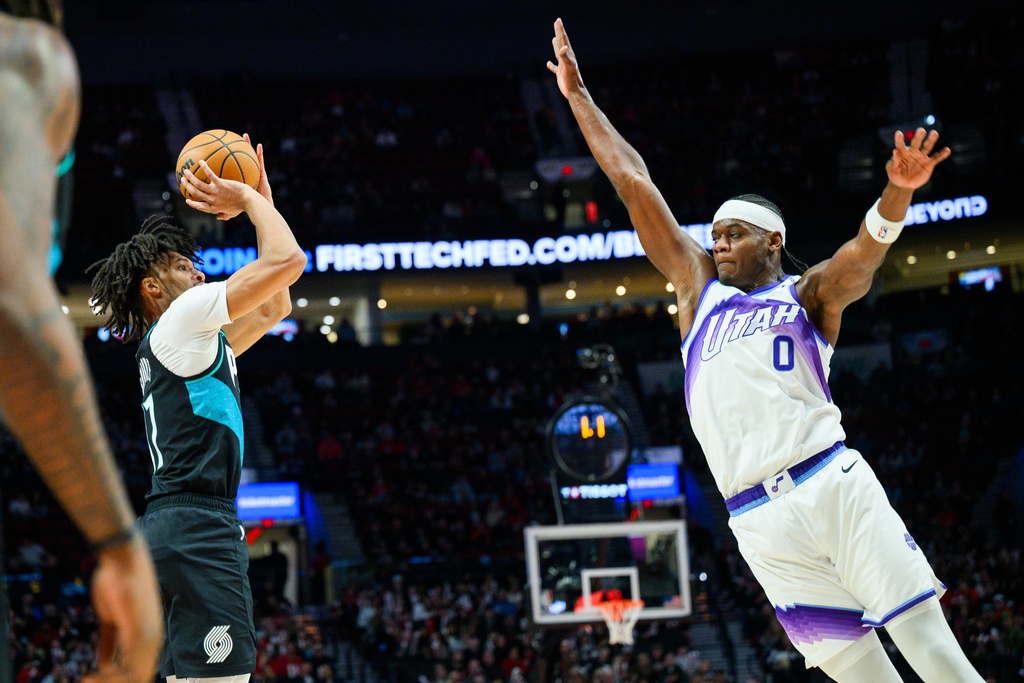 Portland Trail Blazers guard Shaedon Sharpe, left, prepares to shoot a 3-point basket past Utah Jazz forward Taylor Hendricks (0) during the first half of an NBA basketball game, Monday, Jan. 5, 2026, in Portland, Ore. (AP Photo/Molly J. Smith)