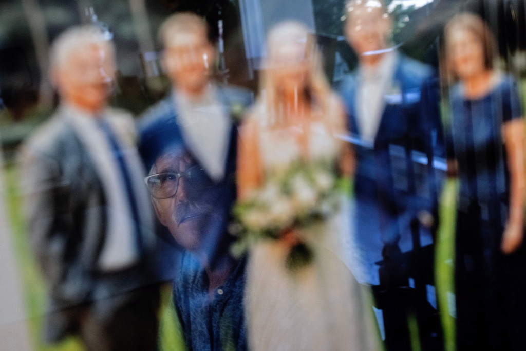Christy Morrill, who lost decades of memories to autoimmune encephalitis, is reflected in a framed family photo at his home, Monday, Aug. 18, 2025, in San Carlos, Calif. (AP Photo/David Goldman)