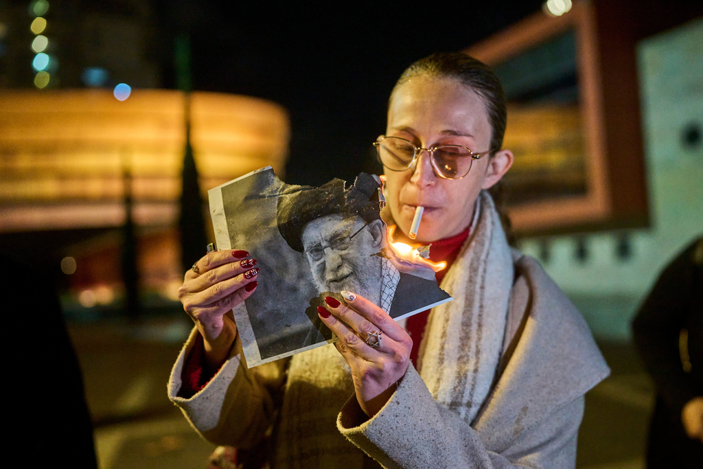 A demonstrator lights a cigarette with a burning poster depicting Supreme Leader Ayatollah Ali Khamenei during a rally in support of Iran's anti-government protests, in Holon, Israel, Wednesday, Jan. 14, 2026. (AP Photo/Ohad Zwigenberg)