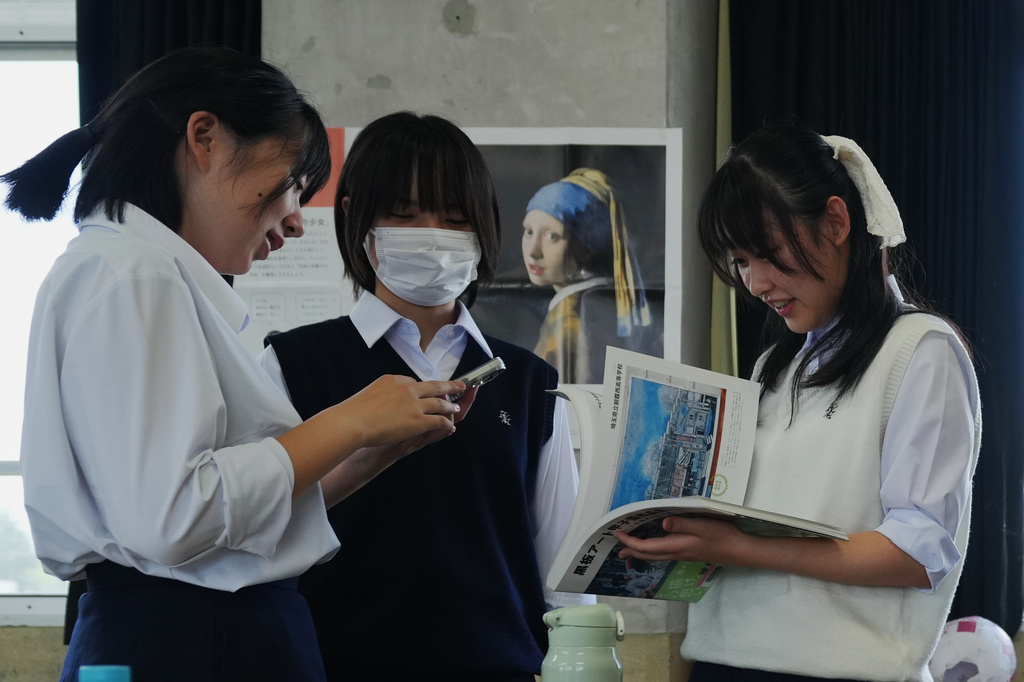 Chiho Ninomiya, from left, Kanami Murata and Karin Makishima, freshman members of the art club at Kumagaya Girls High School, discuss ideas for chalk art drawing at the school in Kumagaya, northwest of Tokyo, Tuesday, July 21, 2026, as they are part of the team participating in a national blackboard art contest. (AP Photo/Hiro Komae)