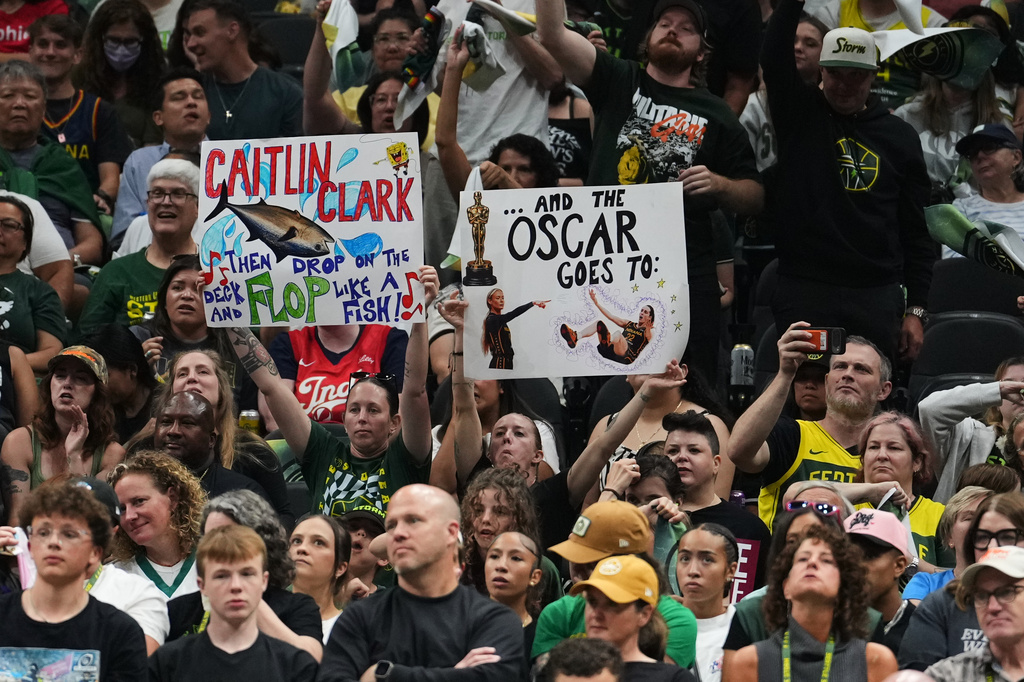 Fans wave signs referencing Indiana Fever guard Caitlin Clark during the second half of a WNBA basketball game between the Seattle Storm and the Indiana Fever, Tuesday, July 28, 2026, in Seattle. (AP Photo/Lindsey Wasson)