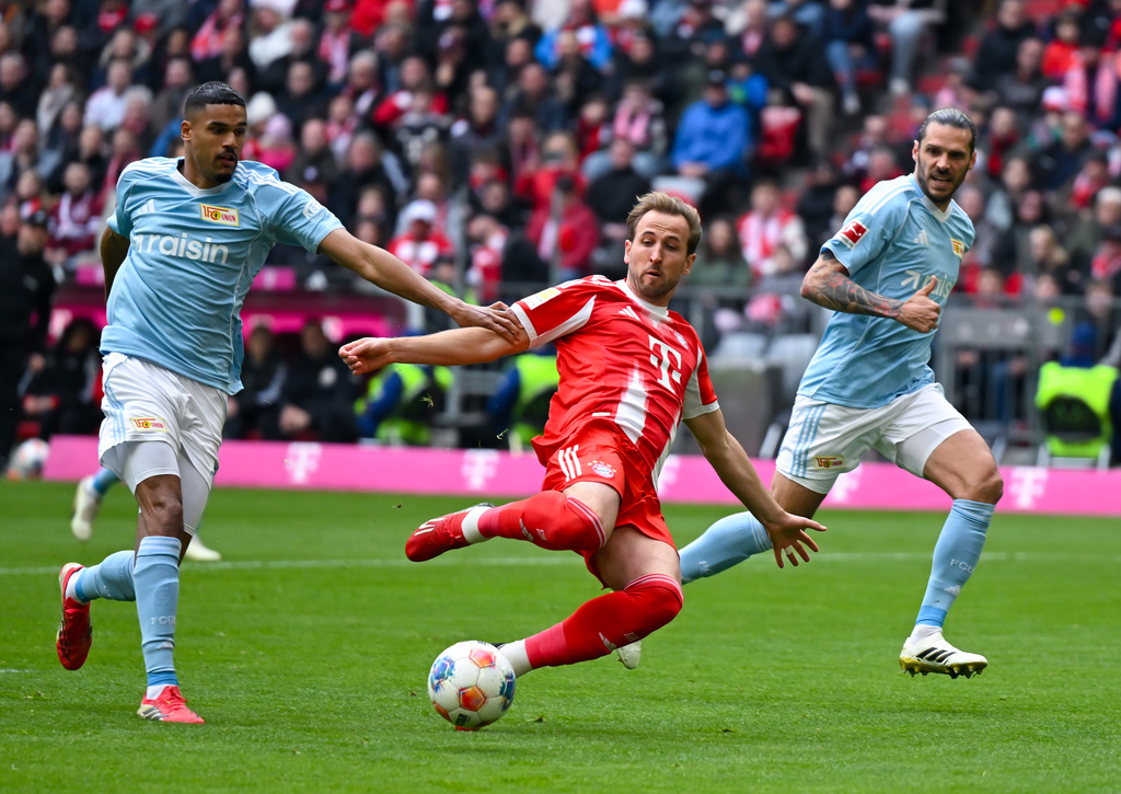 Munich's Harry Kane, center, and Berlin's Livan Burcu, left, challenge for the ball during the German Bundesliga soccer match between FC Bayern Munich and 1. FC Union Berlin in Munich, Germany, Saturday, March 21, 2026 (Sven Hoppe/dpa via AP)