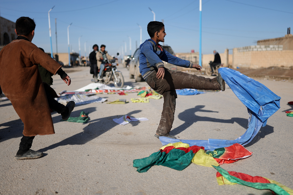 Local youths kick flags belonging to the Syrian Democratic Forces (SDF) in the village of al-Hol in northeastern Syria's Hasakeh province, Syria, Wednesday, Jan. 21, 2026. (AP Photo/Ghaith Alsayed)
