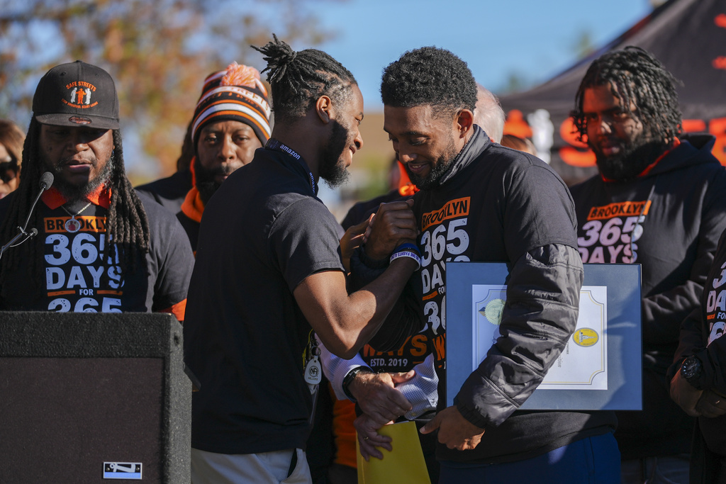 Baltimore Mayor Brandon Scott, right, embraces Adanus Sprillium during a press conference to celebrate achieving over 365 days without a homicide within the Brooklyn neighborhood Safe Streets catchment zone, Tuesday, Nov. 12, 2024, in Baltimore. (AP Photo/Stephanie Scarbrough)