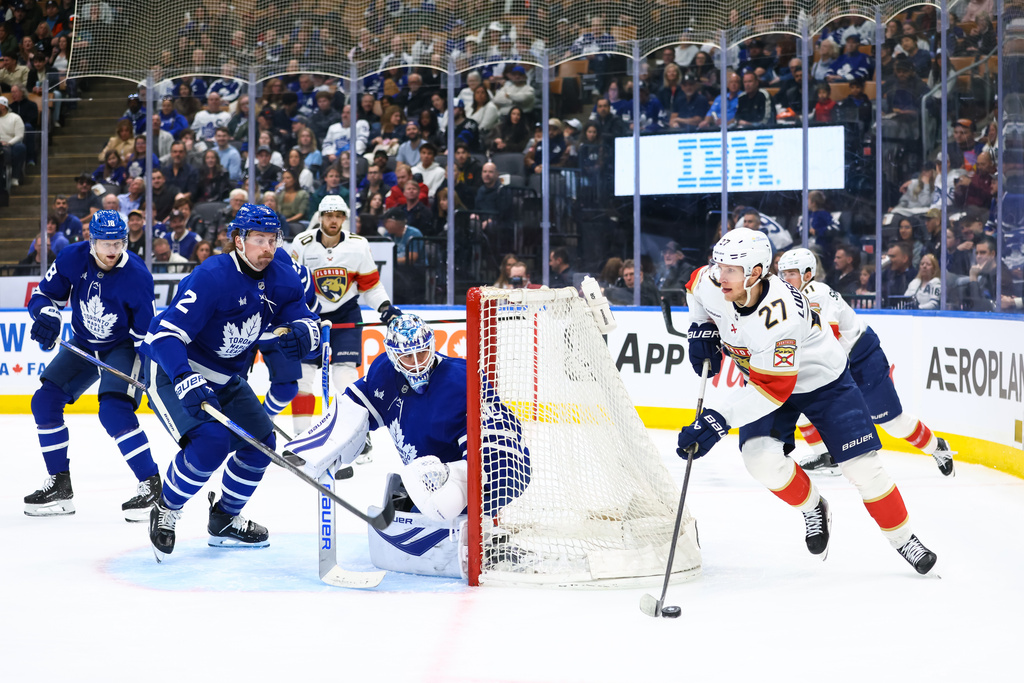 Florida Panthers' Eetu Luostarinen (27) takes the puck around the net as Toronto Maple Leafs' Simon Benoit (2) and goaltender Joseph Woll, center, defend in front of the net during first-period NHL hockey game action in Toronto, Saturday, April 11, 2026. (Cole Burston/The Canadian Press via AP)