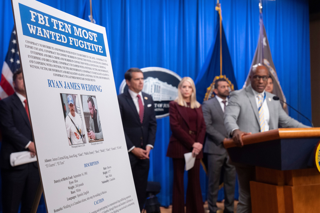 Akil Davis, assistant director in charge of the FBI's Los Angeles Field Office, looks at a wanted poster for Canadian fugitive Ryan James Wedding as he speaks with reporters during a news conference at the Department of Justice, Wednesday, Nov. 19, 2025, in Washington. (AP Photo/Mark Schiefelbein)