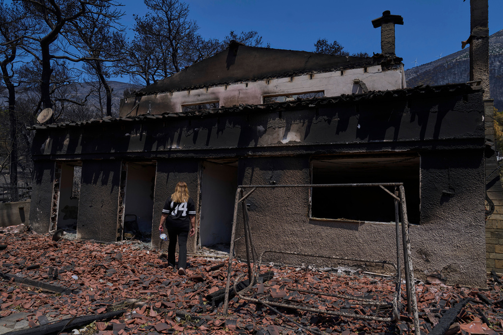 Charoula Spanou walks toward the remains of her holiday home destroyed by a wildfire in Porto Germeno, northwest of Athens, Greece, Tuesday, Aug. 4, 2026. (AP Photo/Petros Giannakouris)