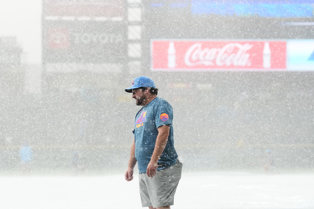 A member of the Coors Field grounds crew stands on the tarpaulin as a storm packing heavy rain and hail sweeps over the stadium before the Colorado Rockies host the Kansas City Royals in a baseball game Friday, July 31, 2026, in Denver. (AP Photo/David Zalubowski)