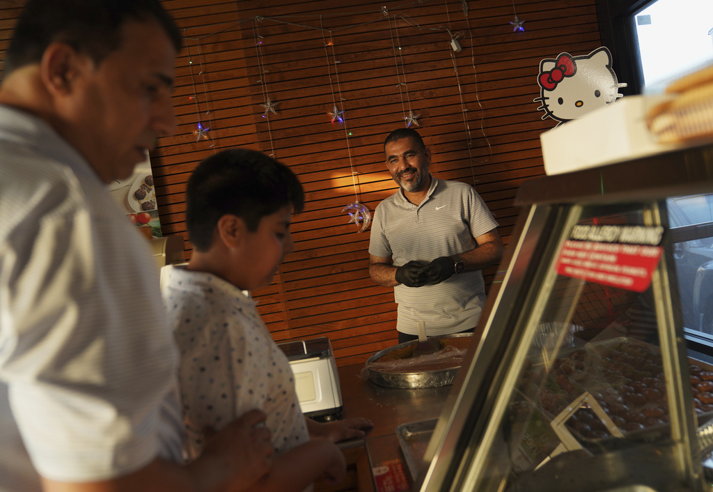 Mohamed Mahmoud, right, helps Afghan refugee Faroz Waziri, left, and his son select deserts at the halal grocery store he opened in 2022 after immigrating from Sudan on Friday, Aug. 8, 2025, in Cedar Rapids, Iowa. (AP Photo/Jessie Wardarski)