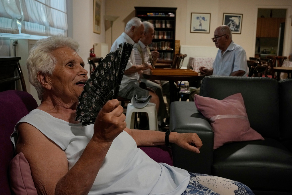 FILE - Jenny Sakellariou uses a hand fan while men play backgammon in an air-conditioned cooling center operated by the Athens municipality throughout a heat wave in Athens, Greece, Aug. 24, 2026. (AP Photo/Thanassis Stavrakis, File)