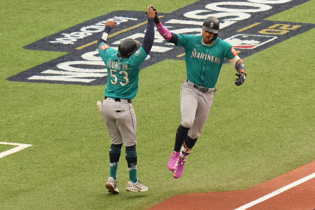 Seattle Mariners' Julio Rodríguez, right, celebrates with first base coach Eric Young Jr. (53) as he rounds the bases after hitting a three-run home against the Toronto Blue Jays during the first inning of Game 2 of baseball's American League Division Series in Toronto, Monday, Oct. 13, 2025. (Chris Young/The Canadian Press via AP)