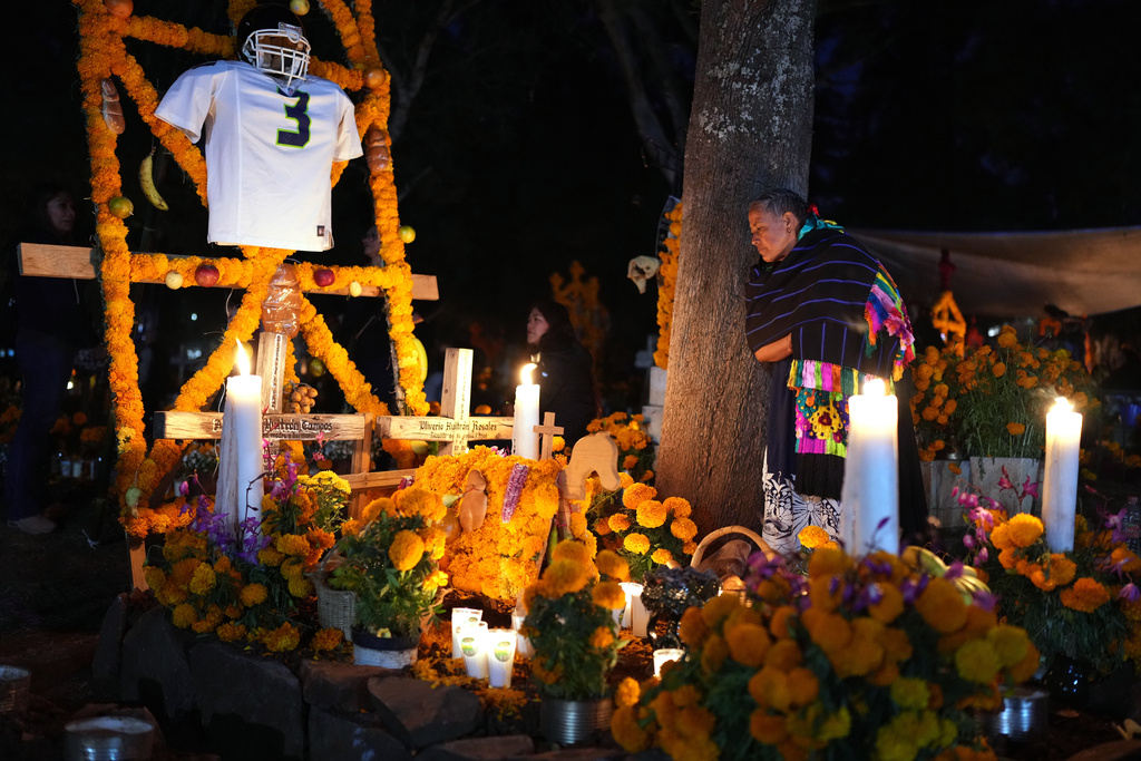 A woman stands next to the grave of a loved one celebrating the Day of the Dead at the cemetery of Tzintzuntzan, Michoacan state, Mexico, Friday, Oct. 31, 2025. (AP Photo/Eduardo Verdugo)