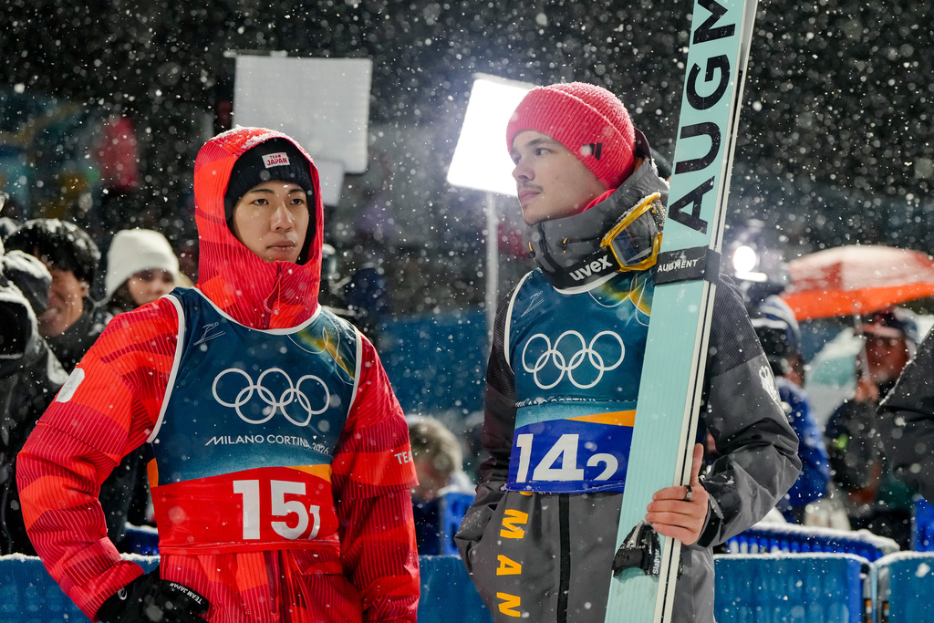 Ren Nikaido, of Japan, left, and Philipp Raimund, of Germany, react as a snowfall interrupts the final round jump of the ski jumping men's super team competition at the 2026 Winter Olympics, in Predazzo, Italy, Monday, Feb. 16, 2026. (AP Photo/Kirsty Wigglesworth)