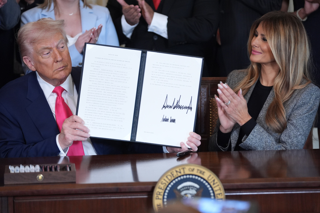 President Donald Trump displays an signed executive order as first lady Melania Trump watches during an event on foster care in the East Room of the at the White House, Thursday, Nov. 13, 2025, in Washington. (AP Photo/Evan Vucci)