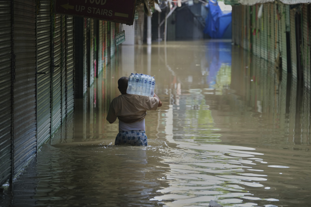 A person wades through flooded water carrying drinking water battles for the residents stuck in their house after the river Yamuna, swollen by incessant rain in the higher regions, overran its banks, in New Delhi, India, Friday, Sept. 5, 2025. (AP Photo/Manish Swarup)