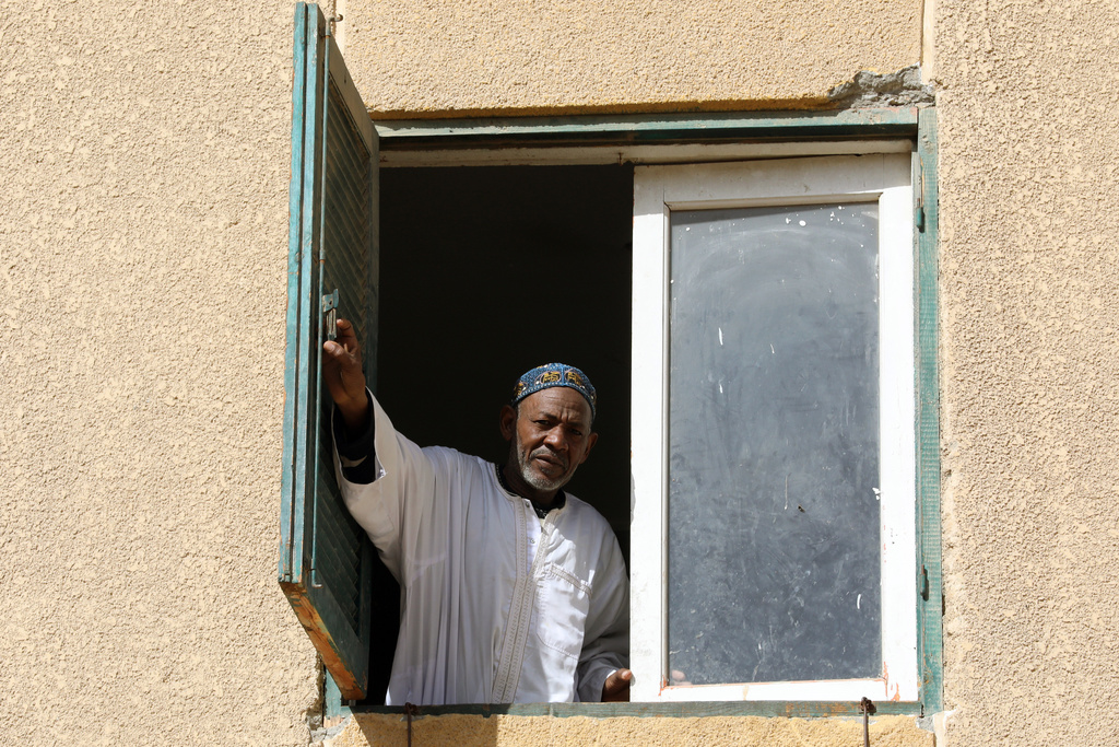 Farouk Abkar, a 60-year-old former charity kitchen worker who spent a year distributing grain and organizing lines at a charity kitchen in Zam Zam refugee camp in Sudan, peers from his home window in 6 October city, Egypt, Wednesday, Jan. 28, 2026. (AP Photo/Khaled el Fiqi)