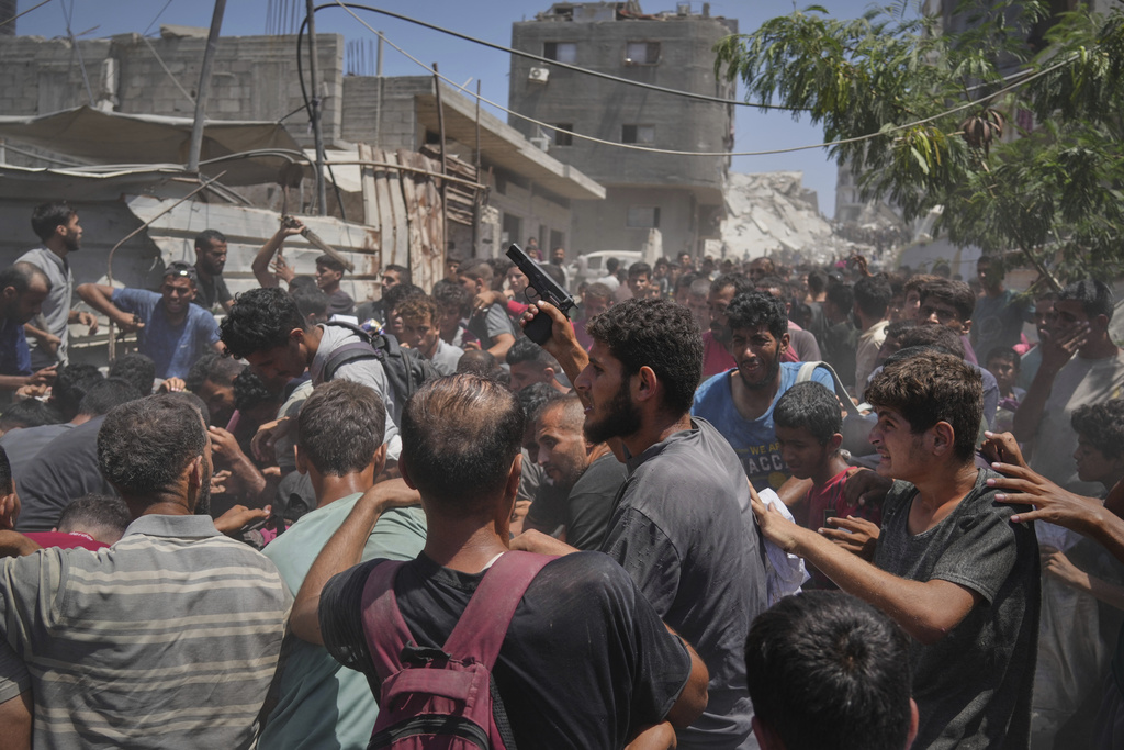 A Palestinian man waves a pistol as others struggle to collect humanitarian aid airdropped into Gaza City, northern Gaza Strip, Aug. 7, 2025. (AP Photo/Jehad Alshrafi)