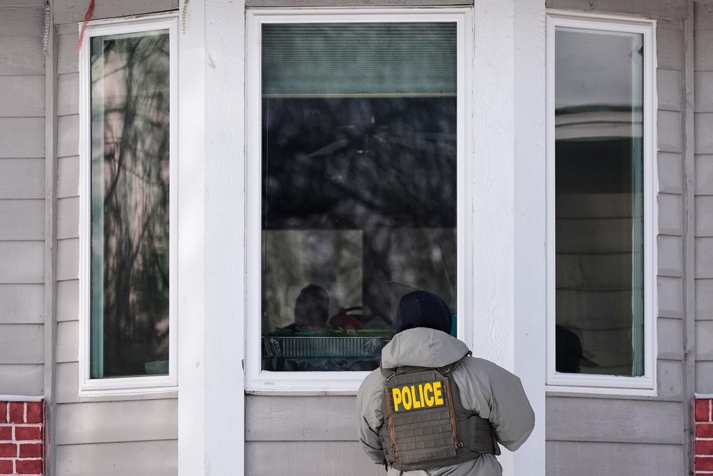 A federal immigration officer looks through a window of a home Tuesday, Jan. 20, 2026, in Maplewood, Minn. (AP Photo/Yuki Iwamura)