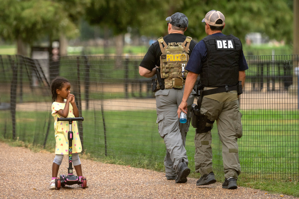 FILE - A child watches as DEA officers patrol along the National Mall in Washington, Aug. 13, 2025. (AP Photo/Mark Schiefelbein, File)