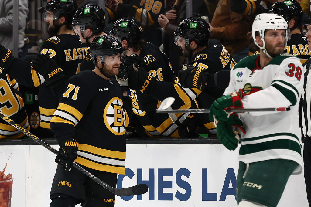 Boston Bruins' Viktor Arvidsson (71) is congratulated at the bench after scoring as Minnesota Wild's Ryan Hartman (38) skates past during the second period of an NHL hockey game Saturday, March 28, 2026, in Boston. (AP Photo/Winslow Townson)