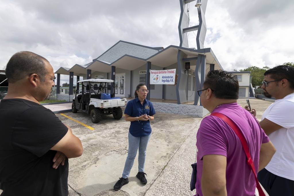 A tour guide talks to visitors outside Parroquia Santísima Trinidad, where Bad Bunny served as an altar boy, in Vega Baja, Puerto Rico, Tuesday, Aug. 12, 2025. (AP Photo/Alejandro Granadillo)
