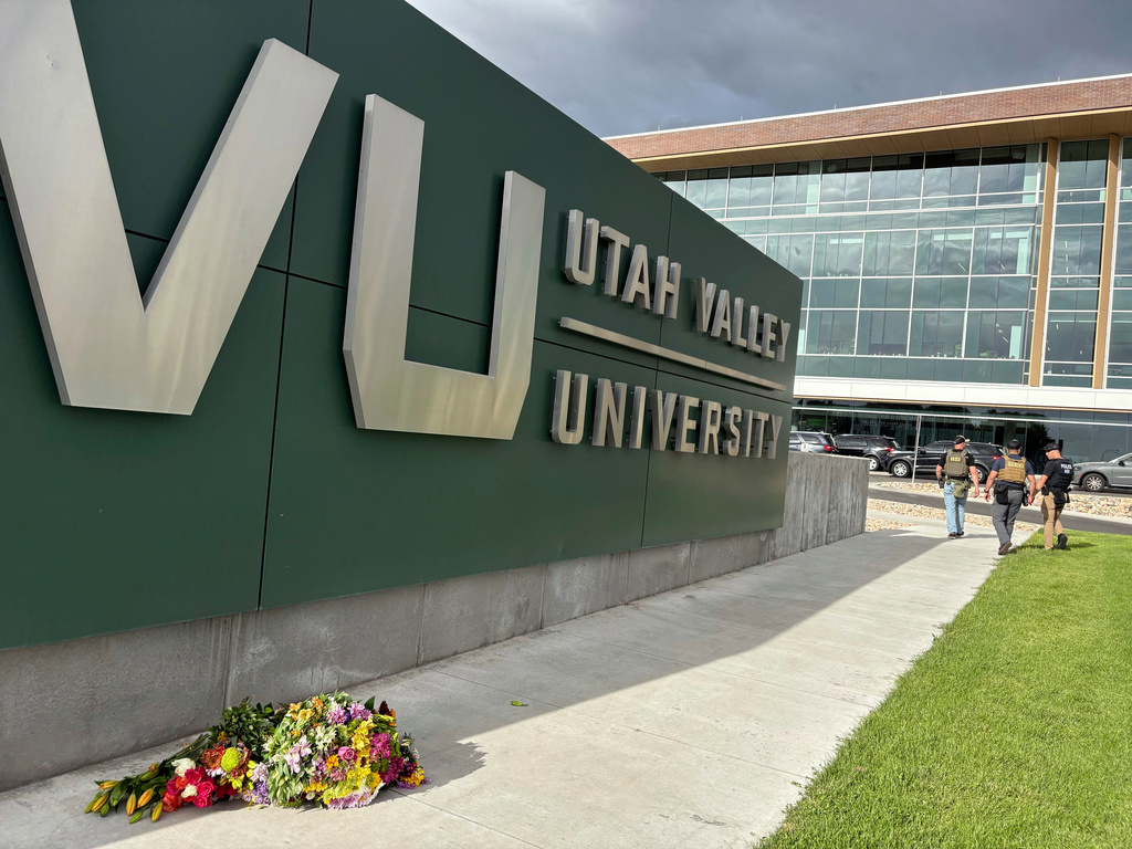 Flowers are shown outside the Keller Building on the Utah Valley University campus as police walk nearby after Charlie Kirk was shot and died during Turning Point's visit to the university, Wednesday, Sept. 10, 2025, in Orem, Utah. (AP Photo/Hannah Schoenbaum)
