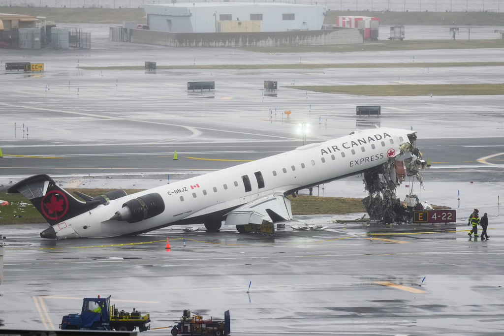 Investigators walk the site, Monday, March 23, 2026, where an Air Canada jet came to rest after colliding with a Port Authority fire truck at LaGuardia Airport, after landing Sunday night in New York. (AP Photo/Seth Wenig)