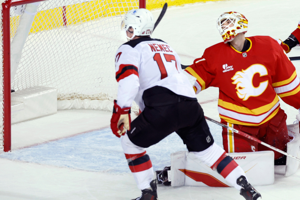 New Jersey Devils' Simon Nemec, left, scores in overtime against Calgary Flames goalie Devin Cooley during NHL hockey game action in Calgary, Alberta, Monday, Jan. 19, 2026. (Larry MacDougal/The Canadian Press via AP)