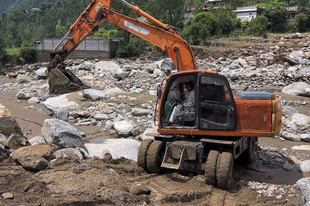 A worker with excavator clear an area filled with rocks after Friday's flash flood hit the area of Qadar Nagar in Buner district, in Pakistan's northwest, Monday, Aug. 18, 2025. (AP Photo/Mohammad Arif)