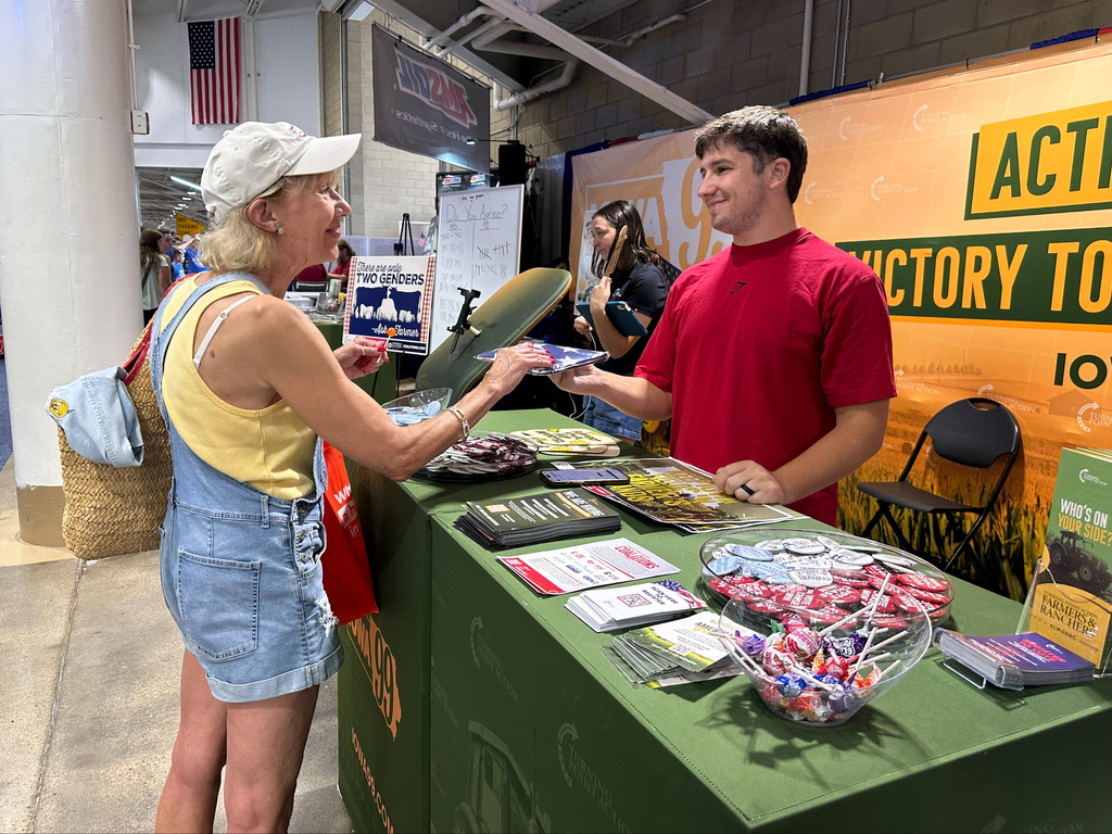 A Turning Point Action staffer gives an American flag to a voter at the Iowa State Fair in Des Moines, Iowa, Friday, Aug. 21, 2026. (AP Photo / Hannah Fingerhut)