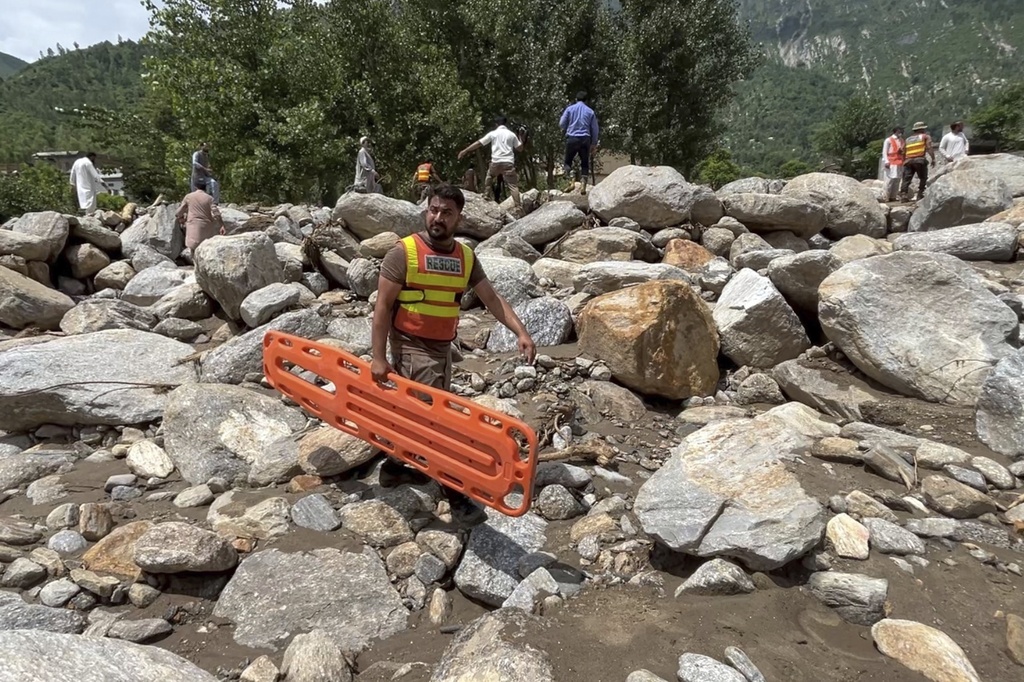 Rescue workers and local cross an area filled with rocks at after Friday's flash flood hit the area of Qadar Nagar in Buner district, in Pakistan's northwest, Monday, Aug. 18, 2025. (AP Photo/Mohammad Arif)