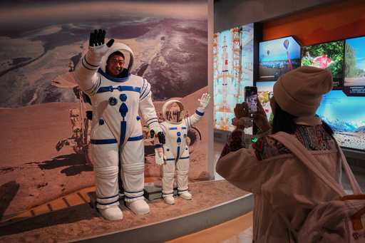 A man poses for a photo shoot with the astronaut figures on display near a picture showing China's Long March 2F rocket for the Shenzhou manned space mission at a museum as China going to send three astronauts for their routine mission to the space station, in Jiayuguan in China's northwestern Gansu province, Wednesday, Oct. 29, 2025. (AP Photo/Andy Wong) A man poses for a photo shoot with the astronaut figures on display near a picture showing China's Long March 2F rocket for the Shenzhou manned space mission at a museum as China going to send three astronauts for their routine mission to the space station, in Jiayuguan in China's northwestern Gansu province, Wednesday, Oct. 29, 2025. (AP Photo/Andy Wong)